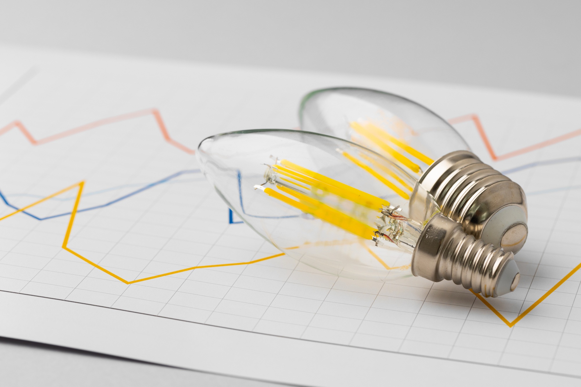 Bombillas LED sobre un gráfico de demanda eléctrica que representa la gestión del consumo energético y la estrategia de Peak Shaving.